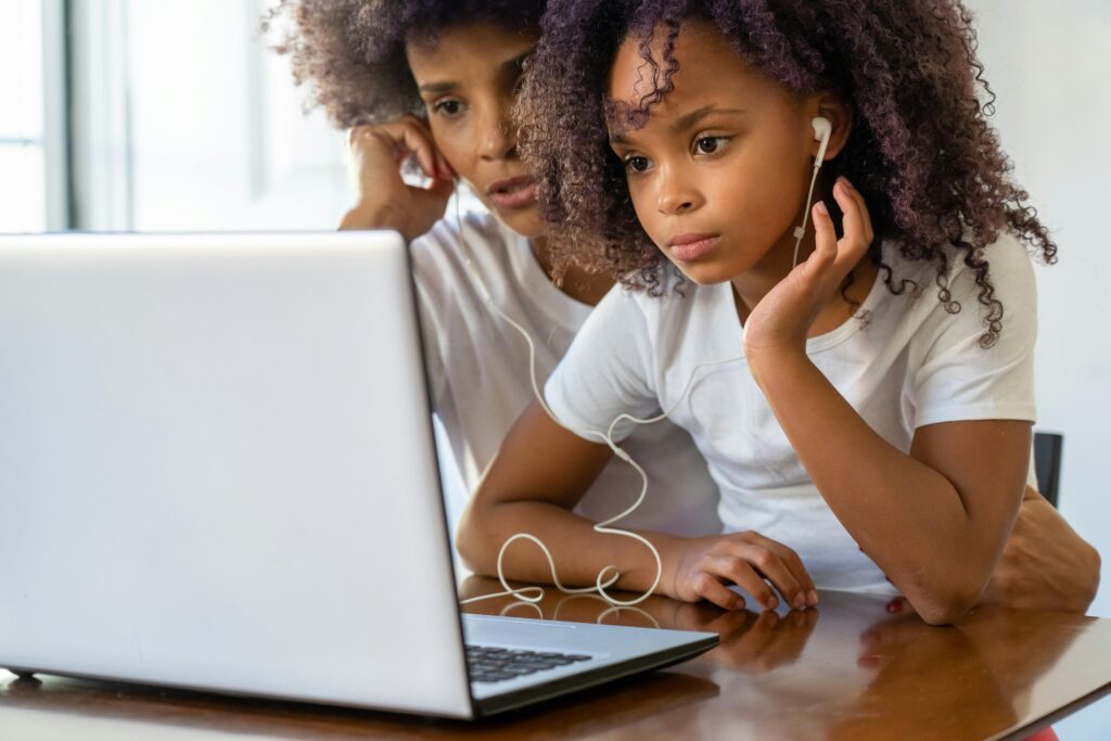 Child and Caregiver Wearing Headphones and Watching A Laptop Together