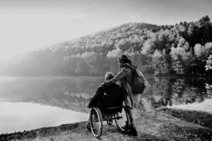 Caregiver With Senior In Wheelchair Enjoying Lake View