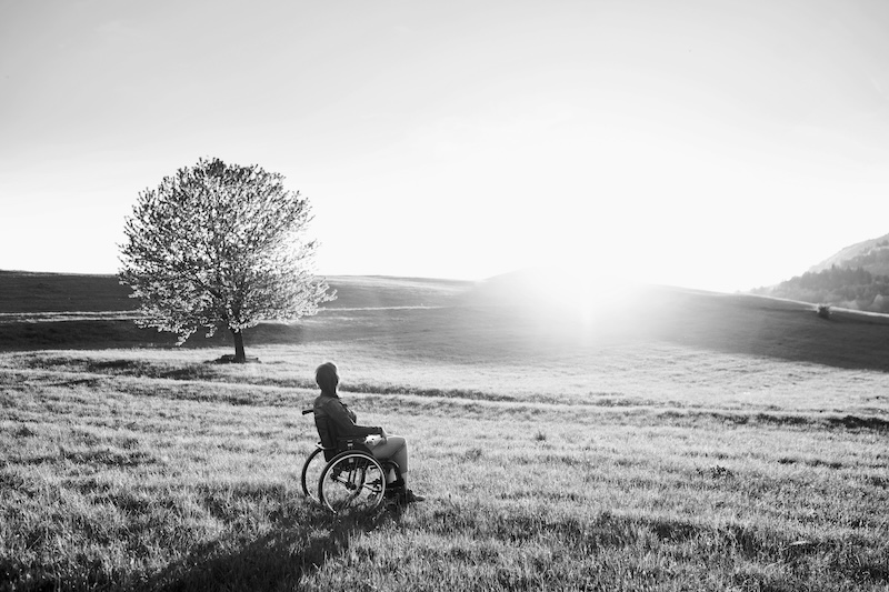 Elderly Person In Wheelchair Looking At Sunset In Field