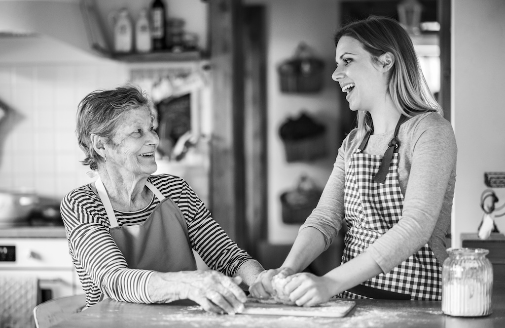 Caregiver And Older Adult Rolling Dough Together In Kitchen